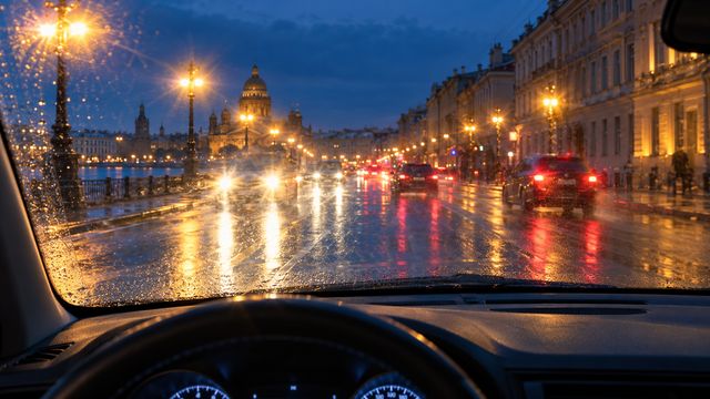 Вечерний вид через мокрое лобовое стекло на яркие фонари и фары